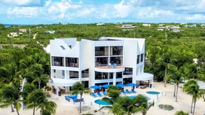 A modern multi-story hotel with a pool area, surrounded by palm trees and a beach. - Altamer Resort (West End Village)