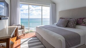 A bedroom with a large bed, a desk, and a chair, with a view of the ocean through a sliding glass door. - Altamer Resort (West End Village)