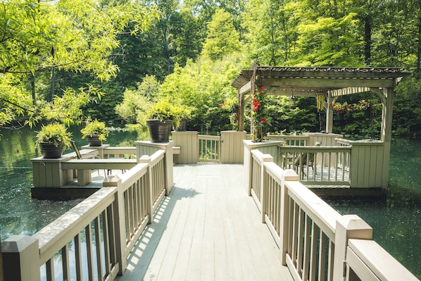 A wooden deck leading to a gazebo over a body of water, surrounded by lush greenery.