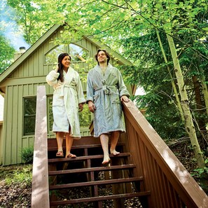 Two individuals in bathrobes standing on a wooden staircase outside a building with a green exterior.