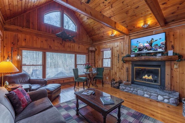 A cozy cabin interior with wooden walls, a fireplace, a large TV, and comfortable seating.