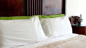 Una cama con almohadas blancas y verdes, una colcha estampada y un cabecero de madera.