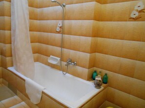 Un baño con bañera, ducha y un estante pequeño con artículos de aseo.