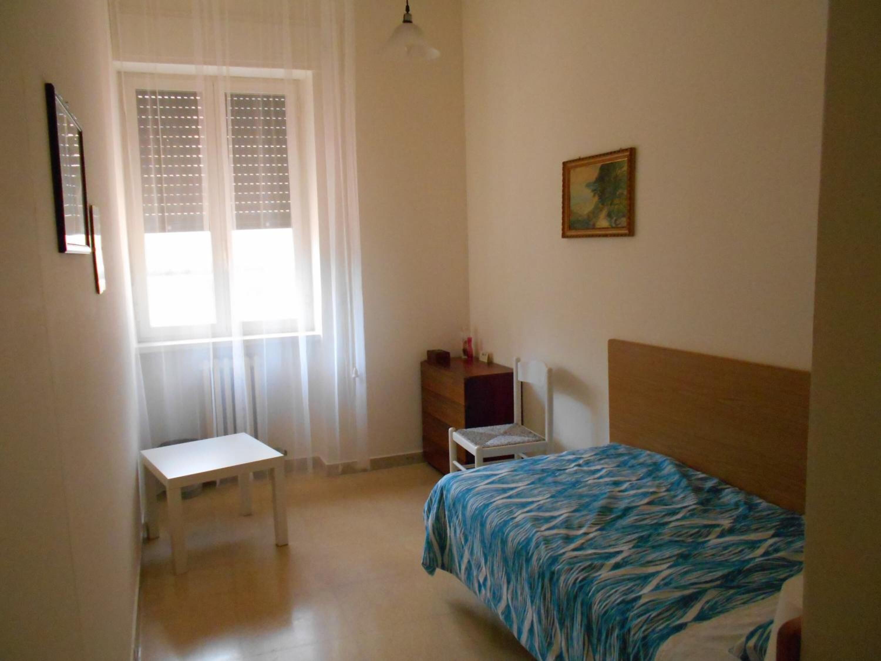 Une chambre à coucher comprenant un lit, un bureau, une chaise, une table de chevet et une fenêtre avec des stores.