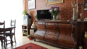 Una sala de estar con pared de ladrillo, un televisor de pantalla plana, un mueble de madera, una mesa de comedor con sillas y una alfombra roja.
