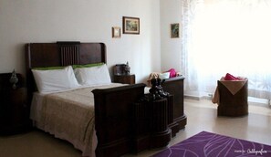 Un dormitorio con una cama grande, una mesita de noche, un aparador y una ventana con cortinas.