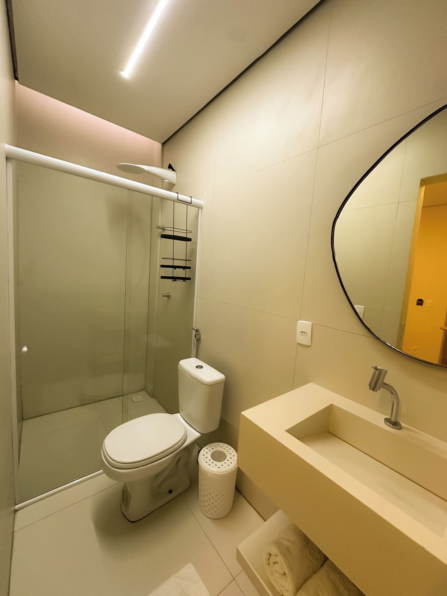 A modern bathroom with a glass-enclosed shower, a toilet, a sink with a mirror, and a towel rack.