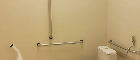 A small, modern bathroom with a toilet, bidet, and handrails.