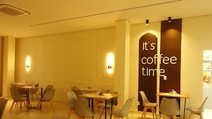 L’intérieur d’un café moderne, avec de nombreuses tables et chaises, une enseigne bien visible indiquant « c’est l’heure du café » et un éclairage chaleureux.