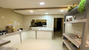 Une cuisine moderne avec des meubles blancs, un îlot central et une étagère intégrée pour ranger les ustensiles de cuisine.