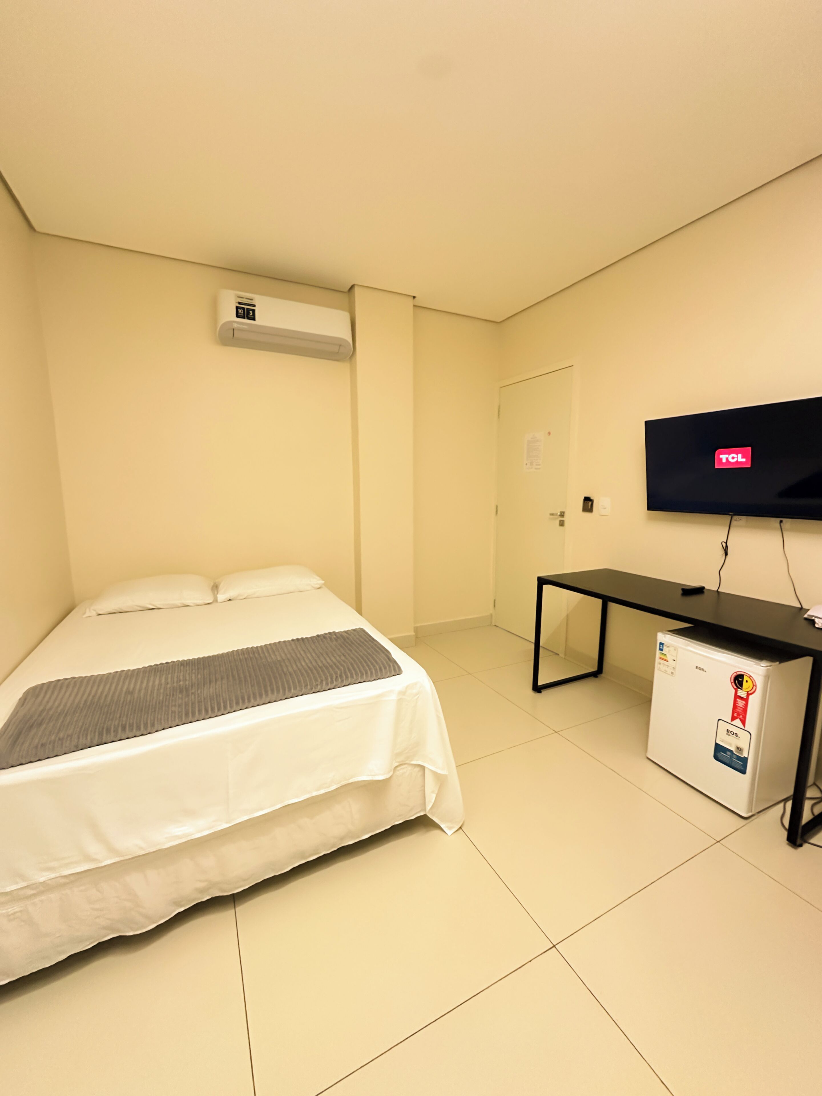 A hotel room with a bed, a TV, a desk, and a refrigerator.