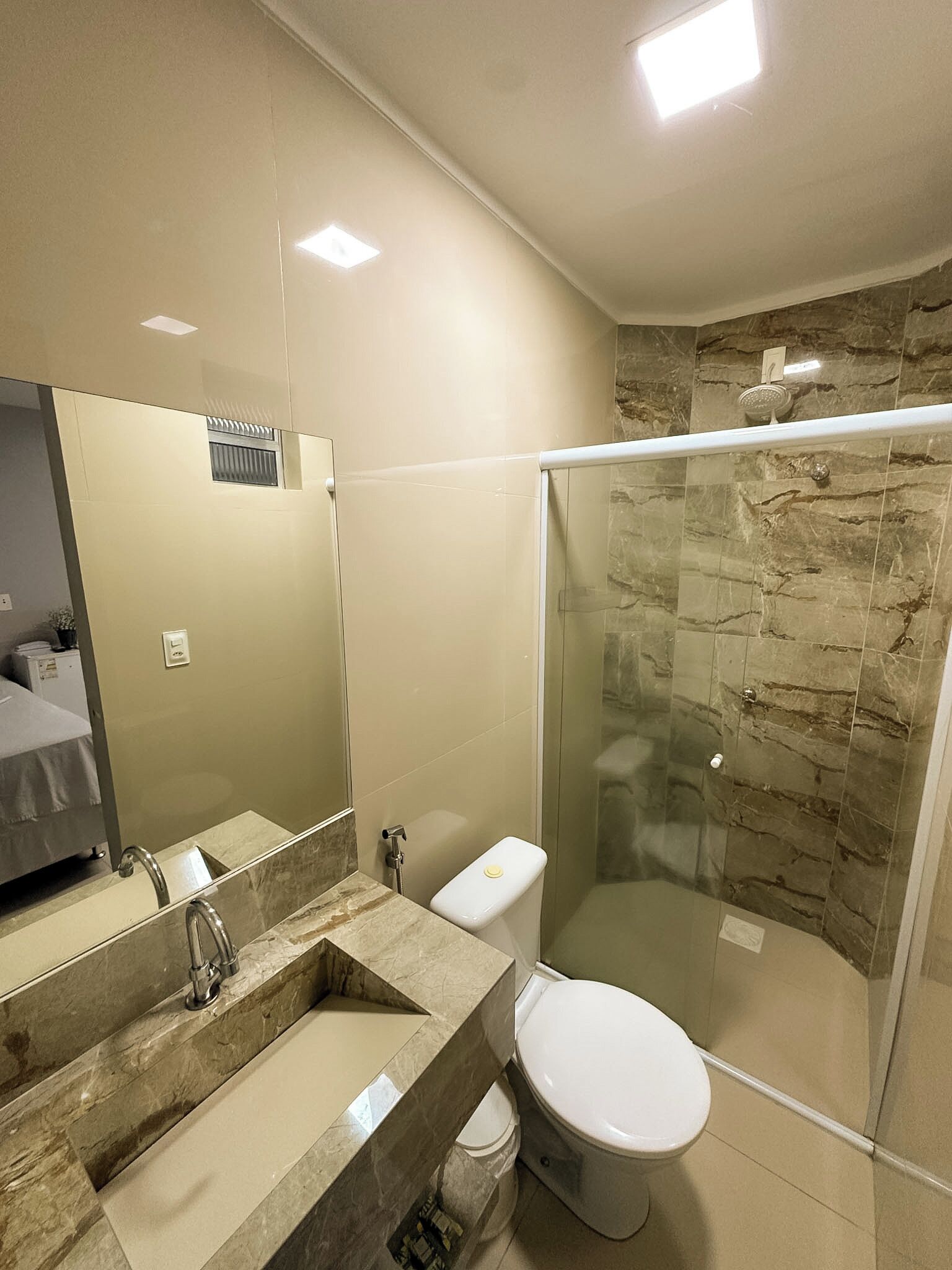A modern bathroom with a glass-enclosed shower, a marble sink, and a toilet.