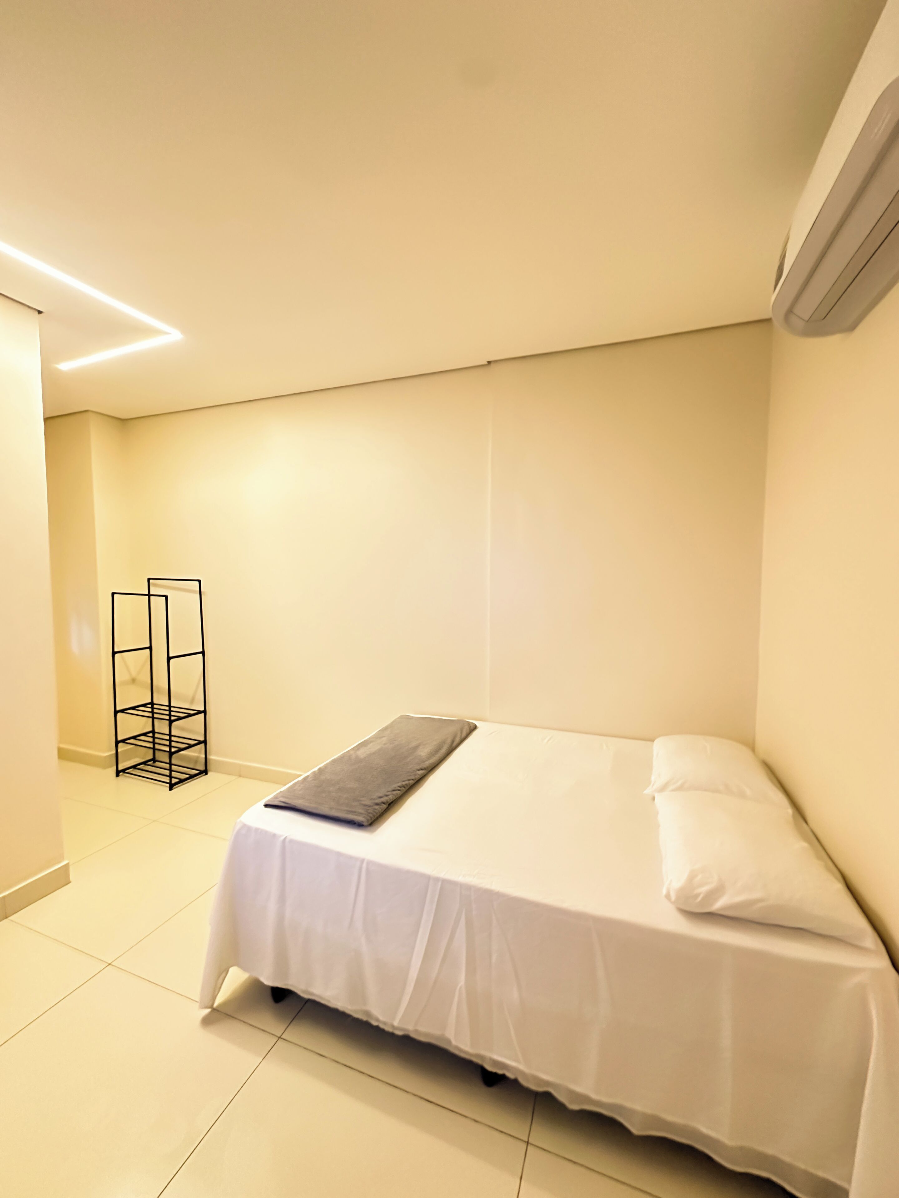 Un dormitorio pequeño y ordenado con una cama individual, una mesita de noche y una lámpara de pie.