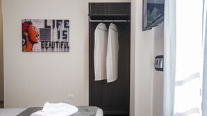 A neatly made bed with a folded white towel, a dark wooden wardrobe, and a wall art piece with the text "LIFE IS BEAUTIFUL". - Garibaldi 136 (Naples)