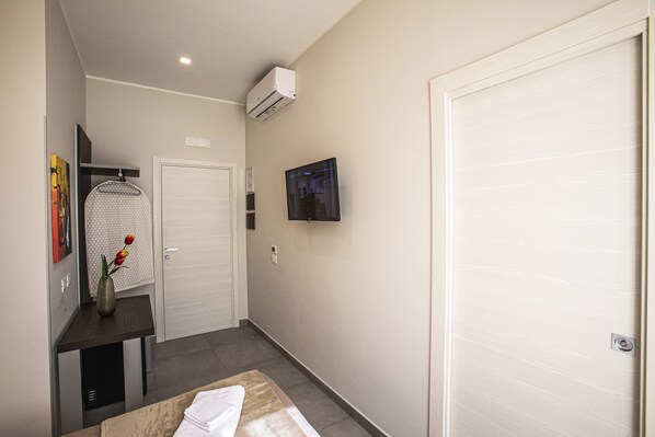 Un couloir d’hôtel avec une porte blanche, un téléviseur à écran plat fixé au mur et une petite table sur laquelle est posé un vase de fleurs.