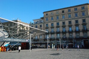 A plaza with a modern glass structure labeled 'Galleria Commerciale' and a historic building in the background. - Garibaldi 136 (Naples)