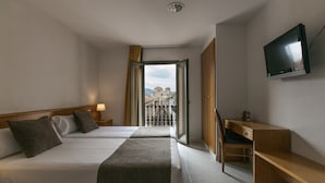 A hotel room with two beds, a desk, a TV, and a balcony with a city view. - Hotel Alta Garrotxa (Tortella)