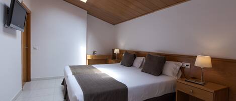 A bedroom with a large bed, wooden headboard, bedside tables with lamps, a flat-screen TV mounted on the wall, and a skylight above the bed.
