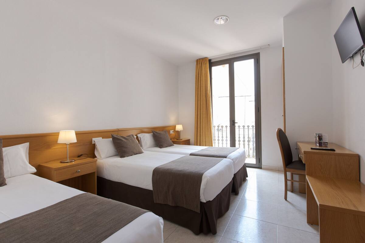 Habitación de hotel con dos camas, un escritorio, una silla, un televisor y una ventana con cortinas.