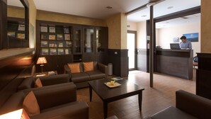 A modern hotel lobby with leather sofas, a coffee table, a reception desk, and a bookshelf with informational brochures. - Hotel Alta Garrotxa (Tortella)