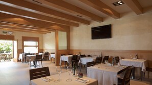 A restaurant with multiple tables, chairs, and a television mounted on the wall. - Hotel Alta Garrotxa (Tortella)