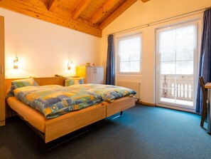 A bedroom with a wooden bed, two bedside lamps, a window with curtains, and a view of a wooden deck outside.