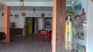 A hotel lobby with a reception desk, a dining area with a red table, and a display of bags and figurines. - Pousada Caminho de Pedras (Cairu)