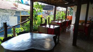 An outdoor patio area with tables and chairs, surrounded by greenery and a view of a residential area. - Pousada Caminho de Pedras (Cairu)