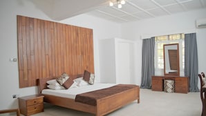 A bedroom with a wooden bed, a nightstand, a dresser, and a mirror. - Lac s Villa (Freetown)