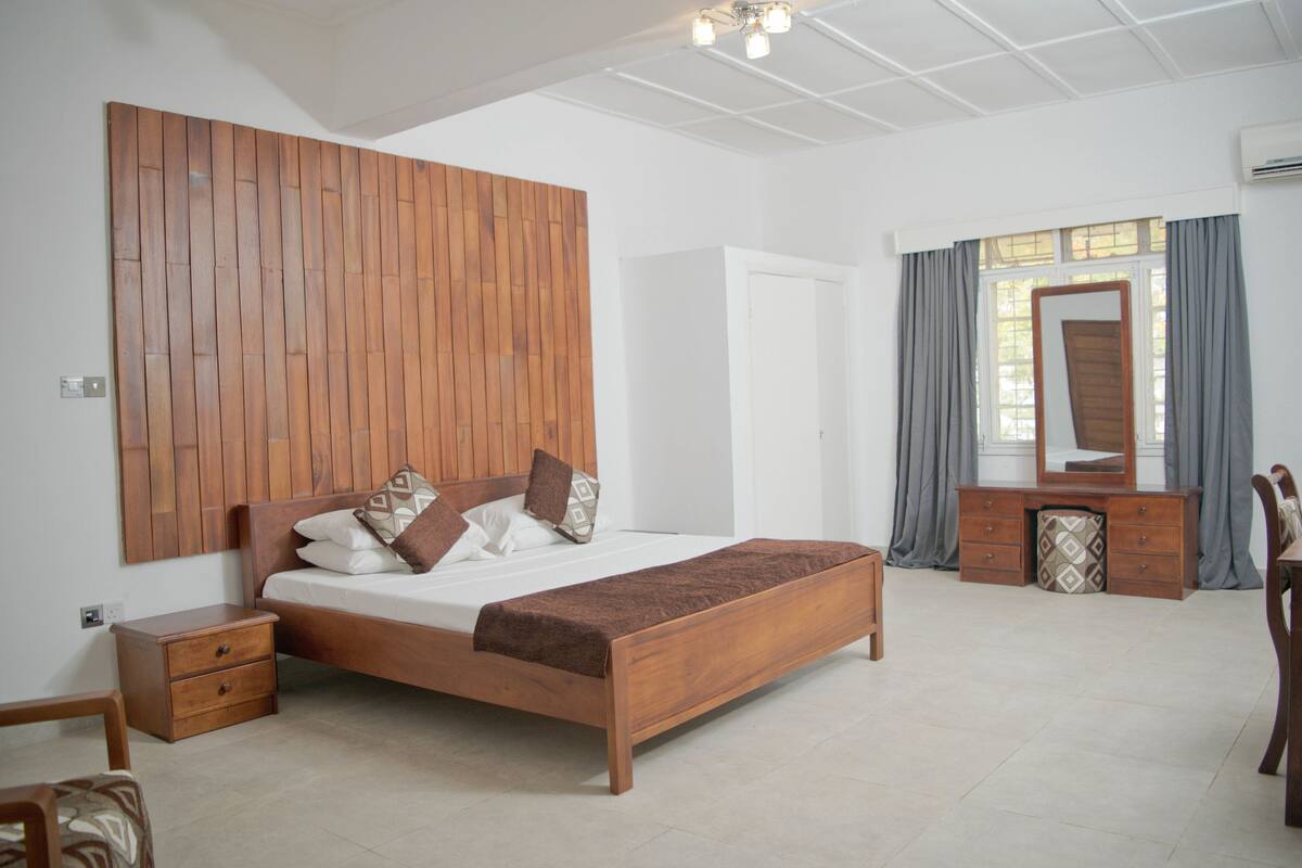 A bedroom with a wooden bed, a nightstand, a dresser, and a mirror.