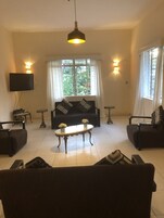 A living room with a sofa, two armchairs, a coffee table, and a TV mounted on the wall.