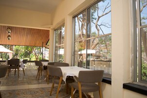 An indoor dining area with large windows, wooden ceiling, and patterned floor tiles.