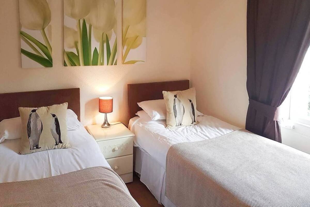 A hotel room with two single beds, a nightstand with a lamp, and a wall with three floral paintings.