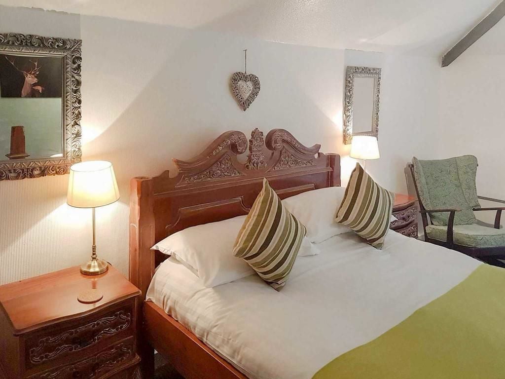 Ein ordentlich bezogenes Bett mit gestreiften Kissen, ein hölzernes Kopfteil, eine Nachttischlampe, ein Sessel und ein Spiegel an der Wand.