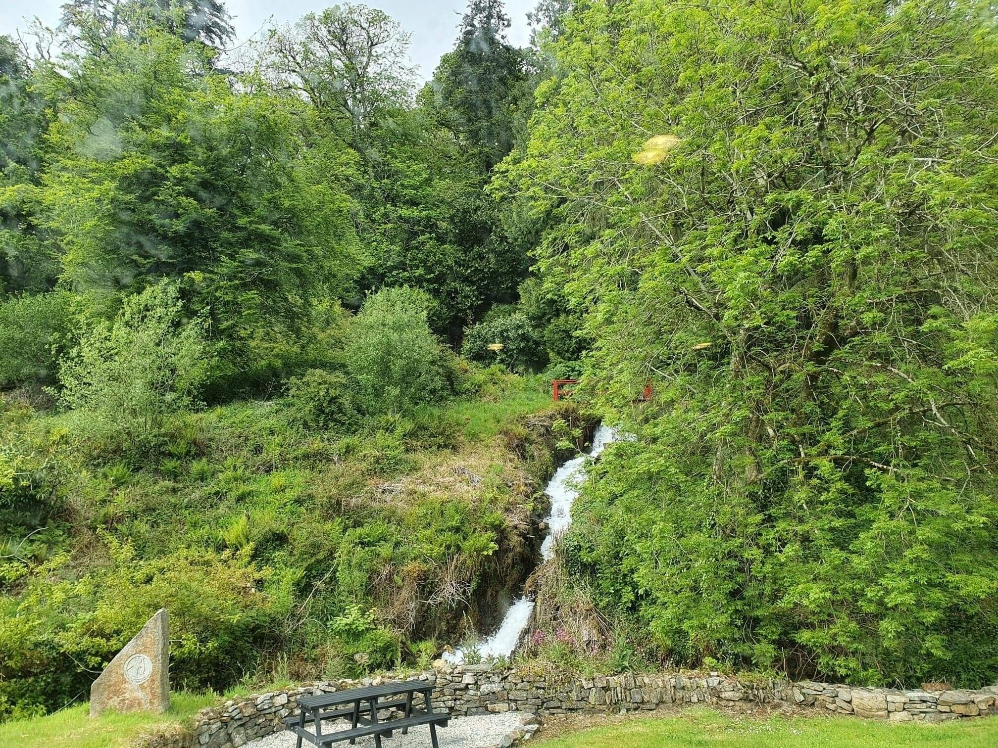 A stone bridge over a small waterfall surrounded by dense greenery.