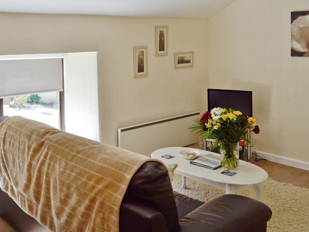 A living room with a sofa, a coffee table with a vase of flowers, and a television on a stand.