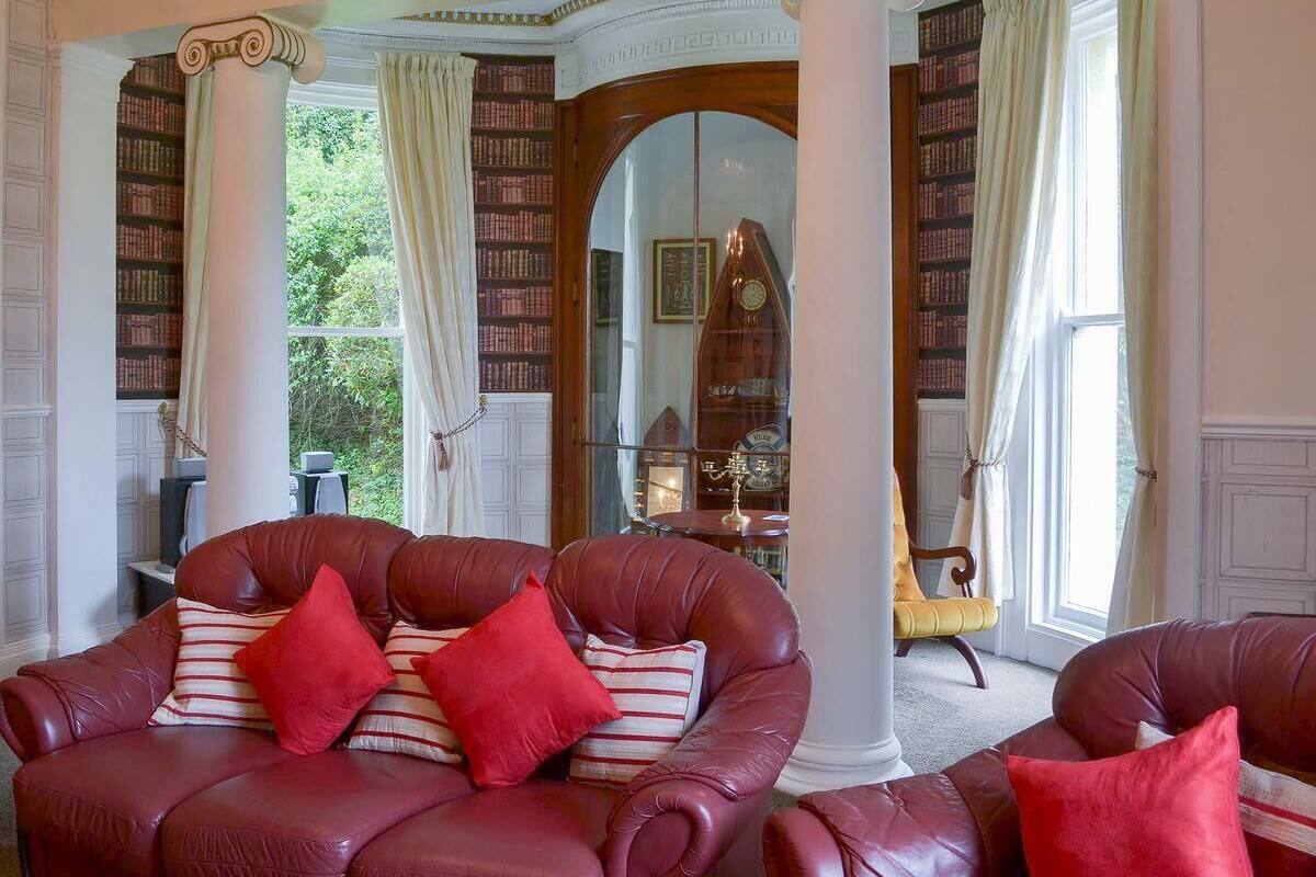 A library with leather armchairs, bookshelves, and a grand piano.