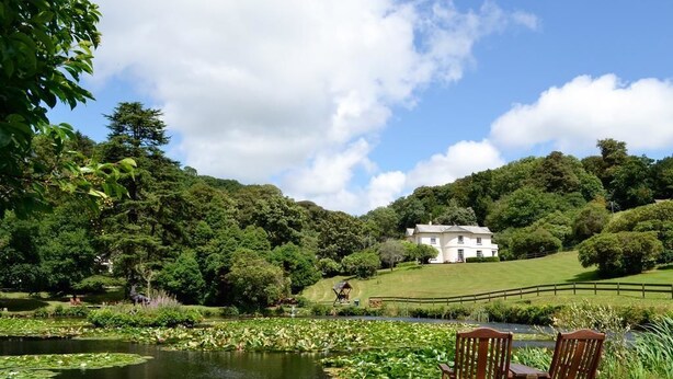 A serene landscape with a pond, two wooden chairs, and a white building in the background.
