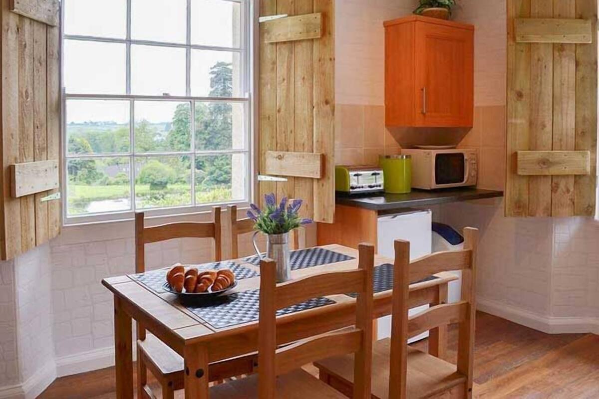 A kitchen with wooden cabinets, a window with a view of greenery, and a table with a bowl of bread.