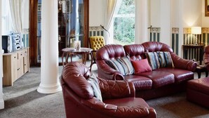 A luxurious living room with leather sofas, a wooden cabinet, and a large window with curtains.
