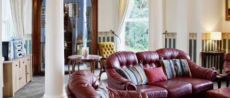 A luxurious living room with leather sofas, a wooden cabinet, and a large window with curtains.