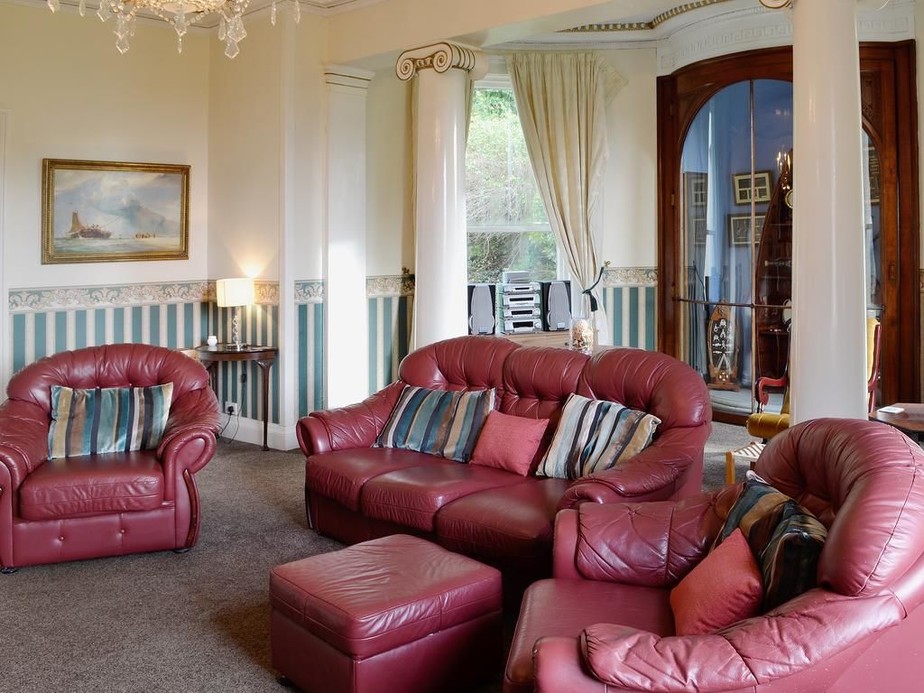 A room with a large red leather sofa set, a chandelier, and a view of the outdoors through a window.