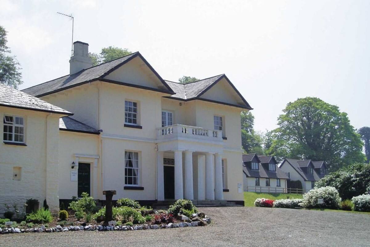 A large, two-story building with a symmetrical facade, a central entrance with columns, and a gravel driveway.