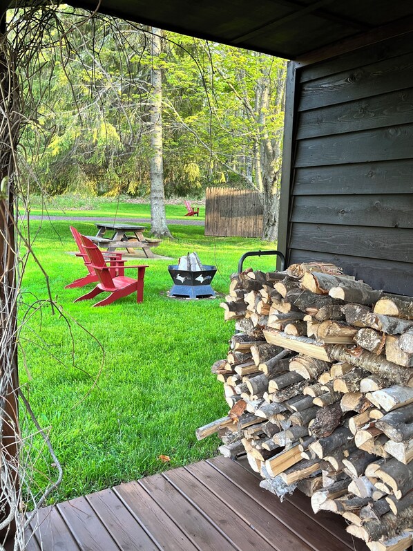 A wooden deck with a stack of firewood, a picnic table with red chairs, and a wooden fence in a backyard.
