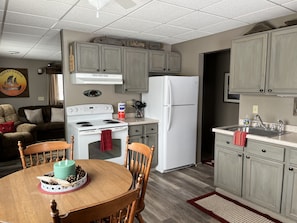 A kitchen with a stove, refrigerator, and wooden cabinets. There is a dining table with chairs and a small decorative item on it.