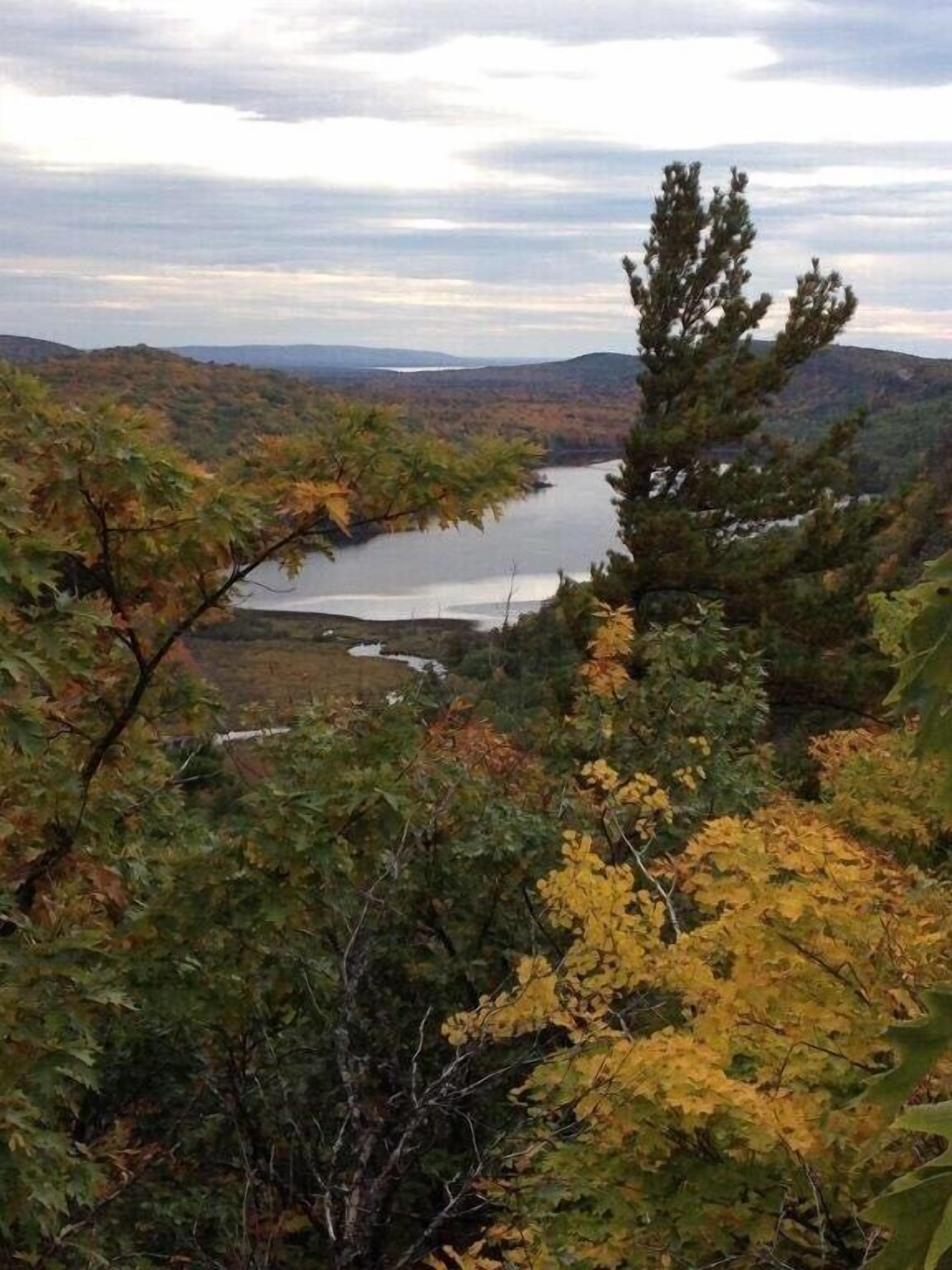 Un paysage naturel avec un lac entouré d’arbres et de collines.
