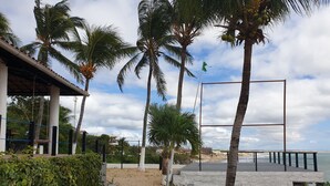 Zona de playa con muelle de madera, palmeras y vista al mar.