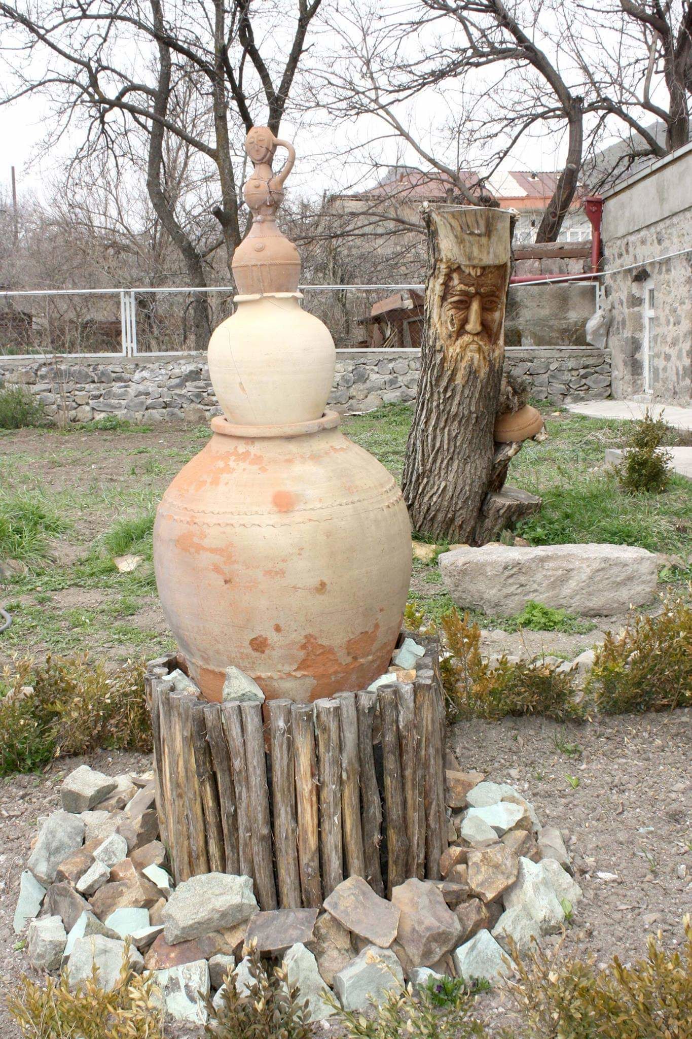 Une grande urne en céramique, posée sur un tronc d’arbre et entourée de rochers.