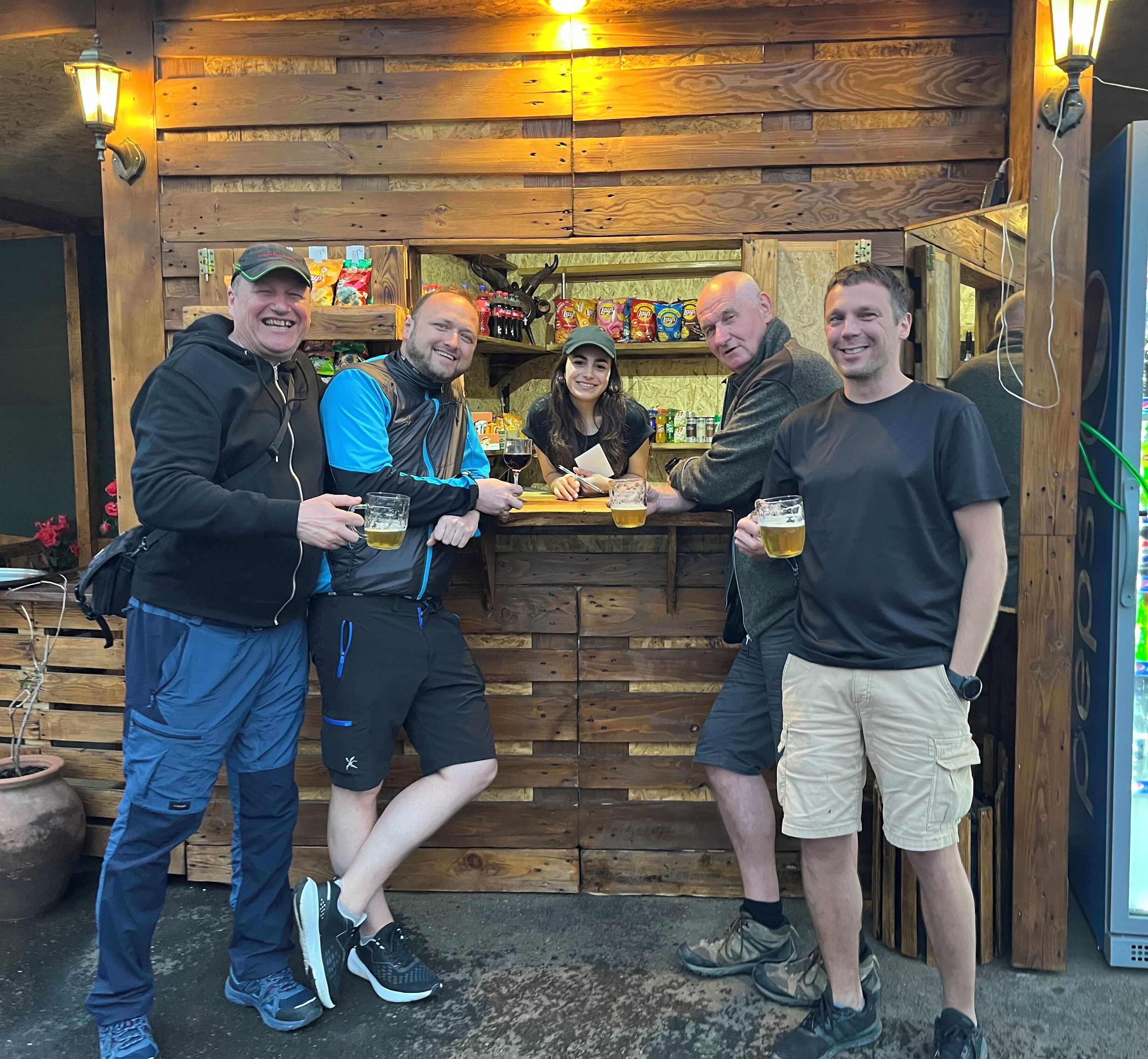 A group of people standing outside a wooden building with a bar area.