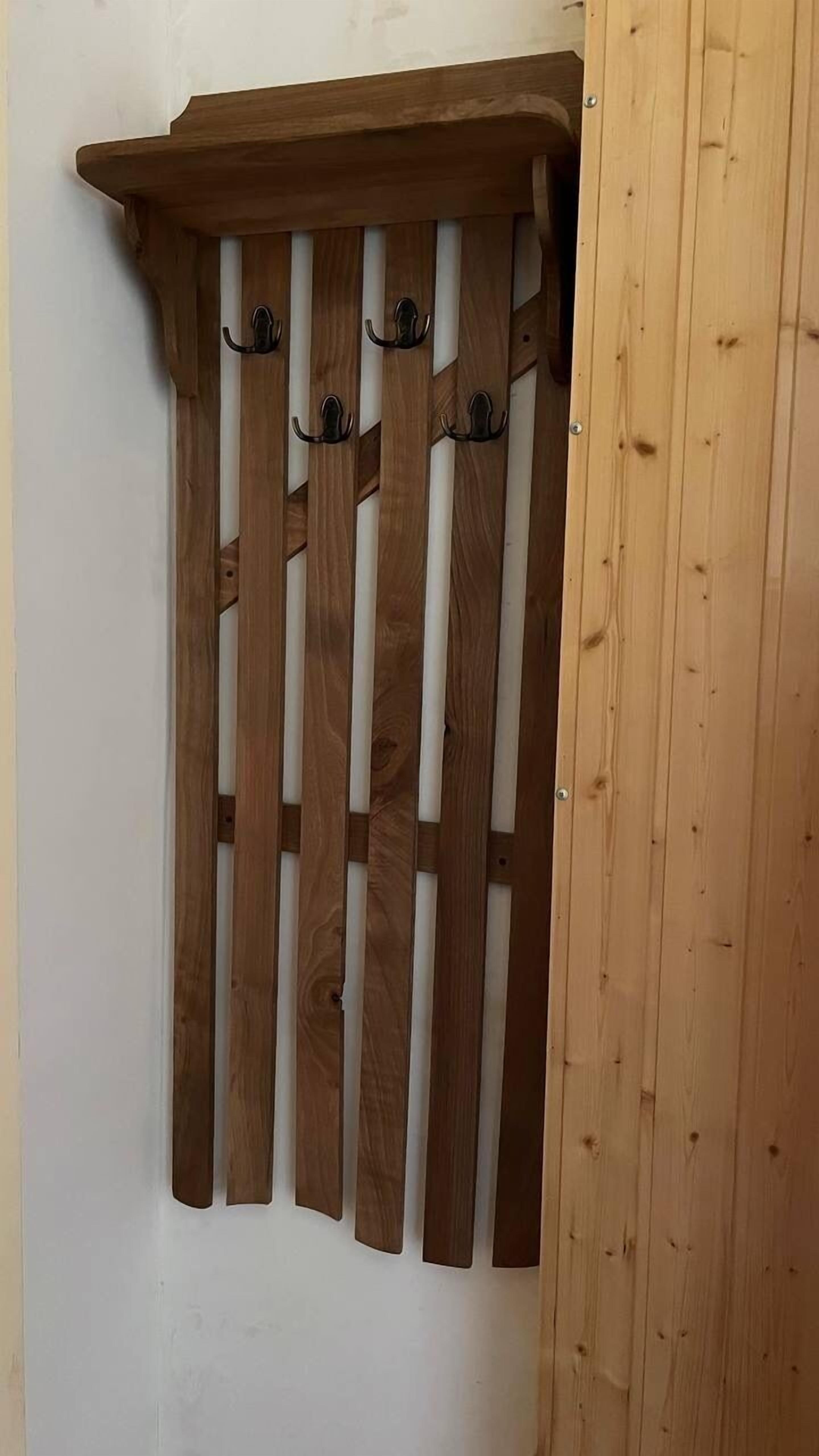 Un perchero de madera con varios ganchos frente a una pared blanca.